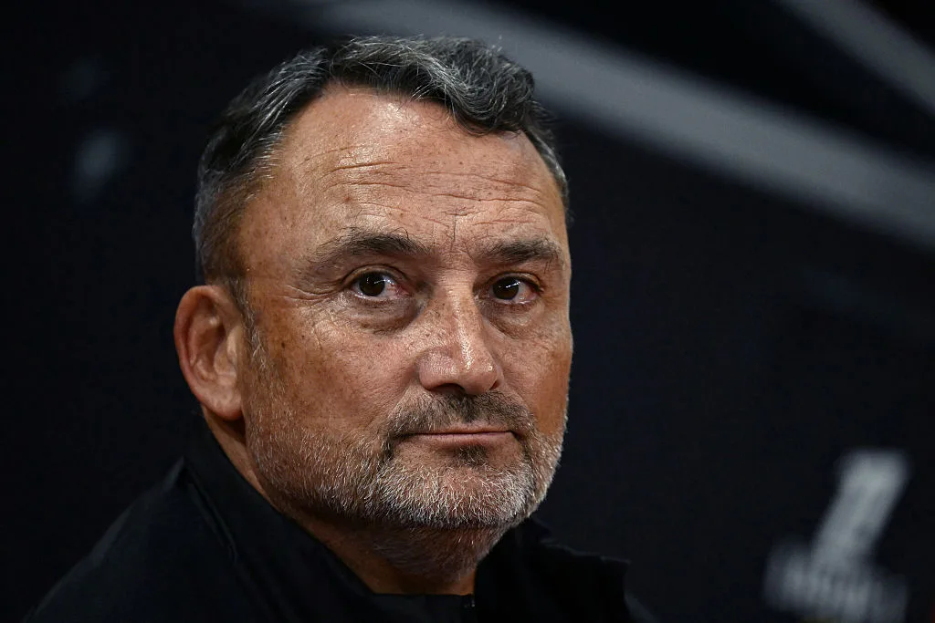 Close-up portrait of a serious-looking middle-aged man with short dark hair and a trimmed beard.
