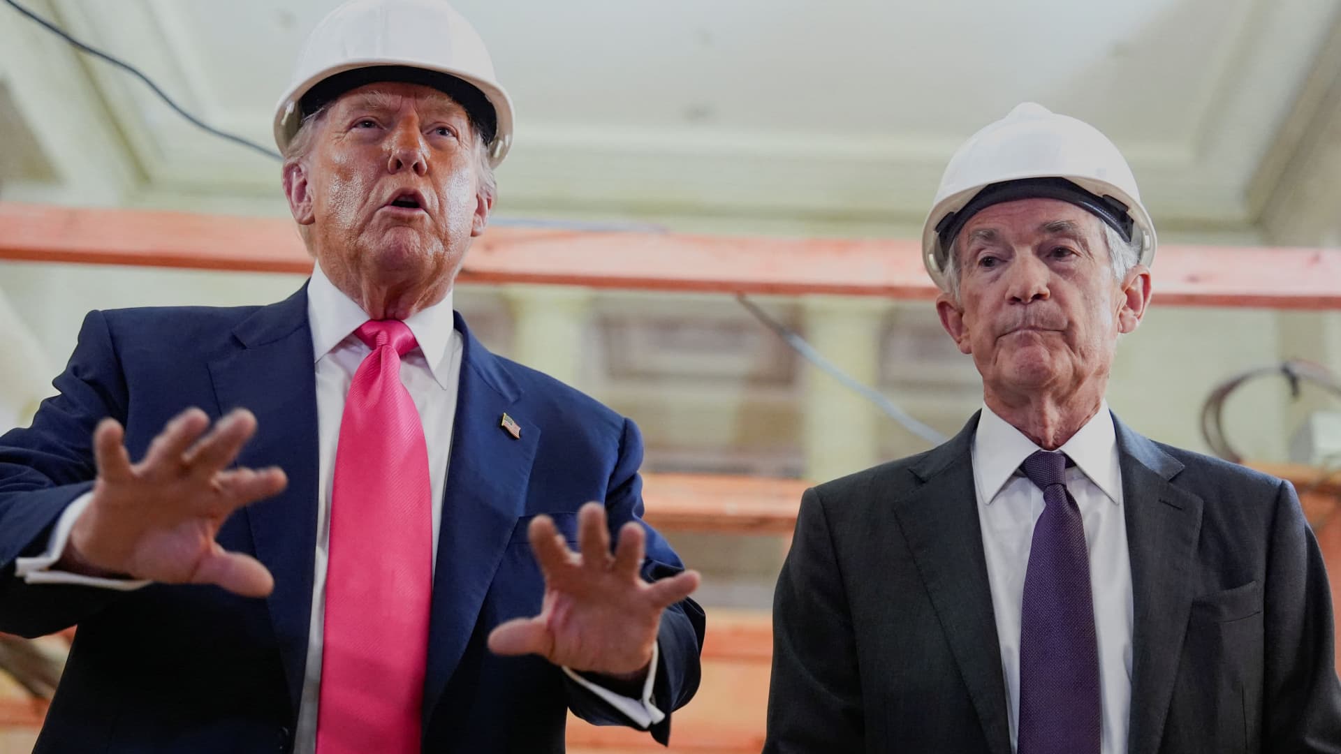 Two men in suits and white hard hats stand inside a building under renovation.
