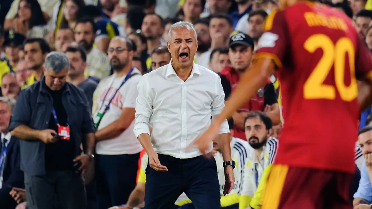 Football coach in white shirt gesturing on sideline as players and spectators watch