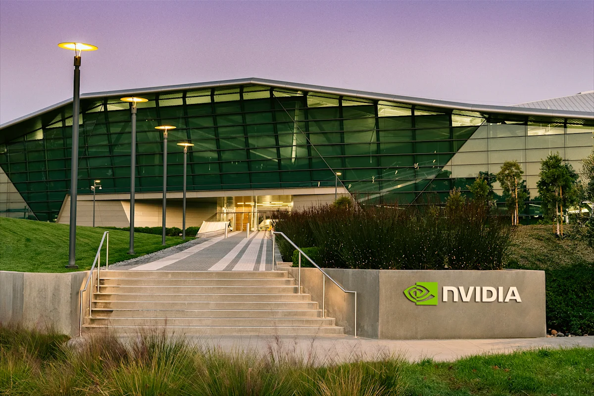 Exterior of a modern glass building with illuminated NVIDIA signage beside landscaped steps