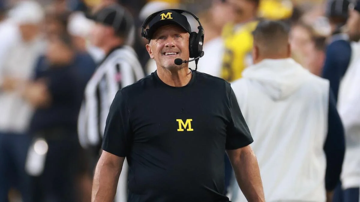 Football coach in Michigan gear and headset standing on the sideline during a game