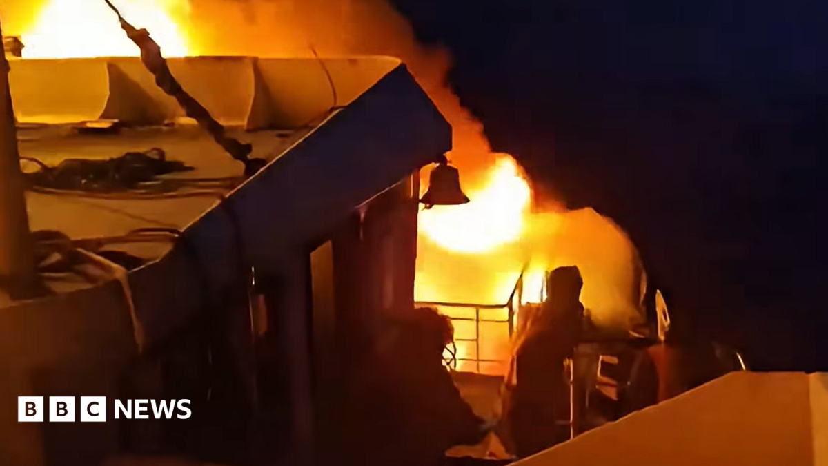 Nighttime ferry fire with flames and thick smoke behind silhouetted people on deck