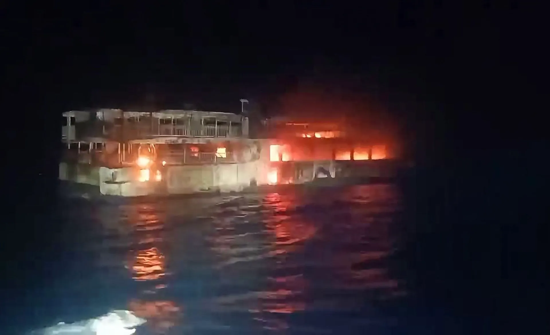 Nighttime ferry engulfed in flames, with smoke rising and firelight reflecting on the water.