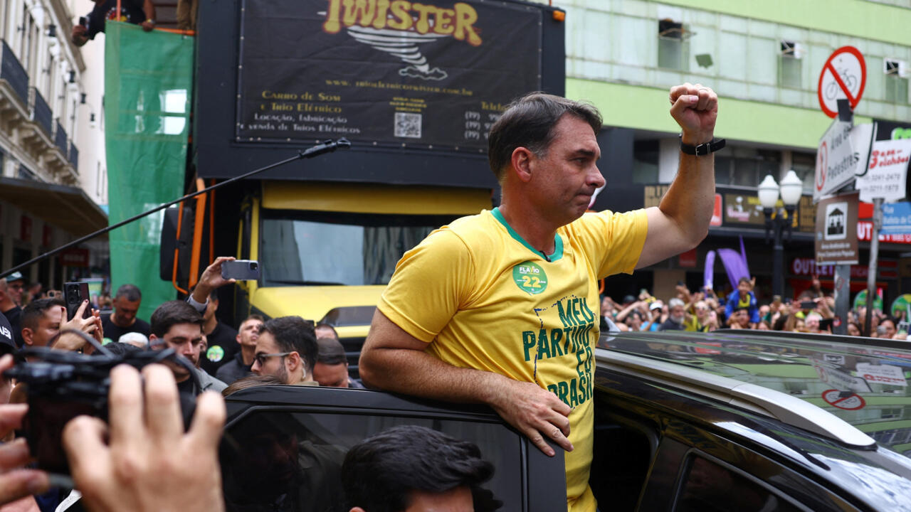 Man in yellow shirt raises a fist while standing through a car roof amid a crowd.