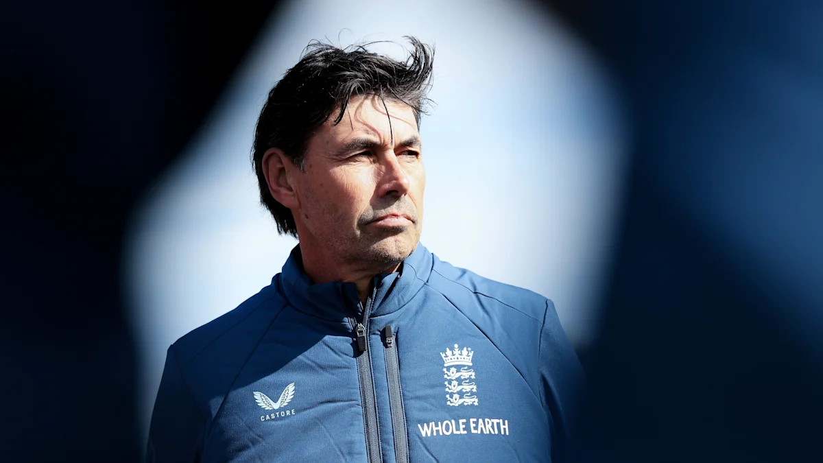 Man in blue England training jacket standing under bright lights against a dark background