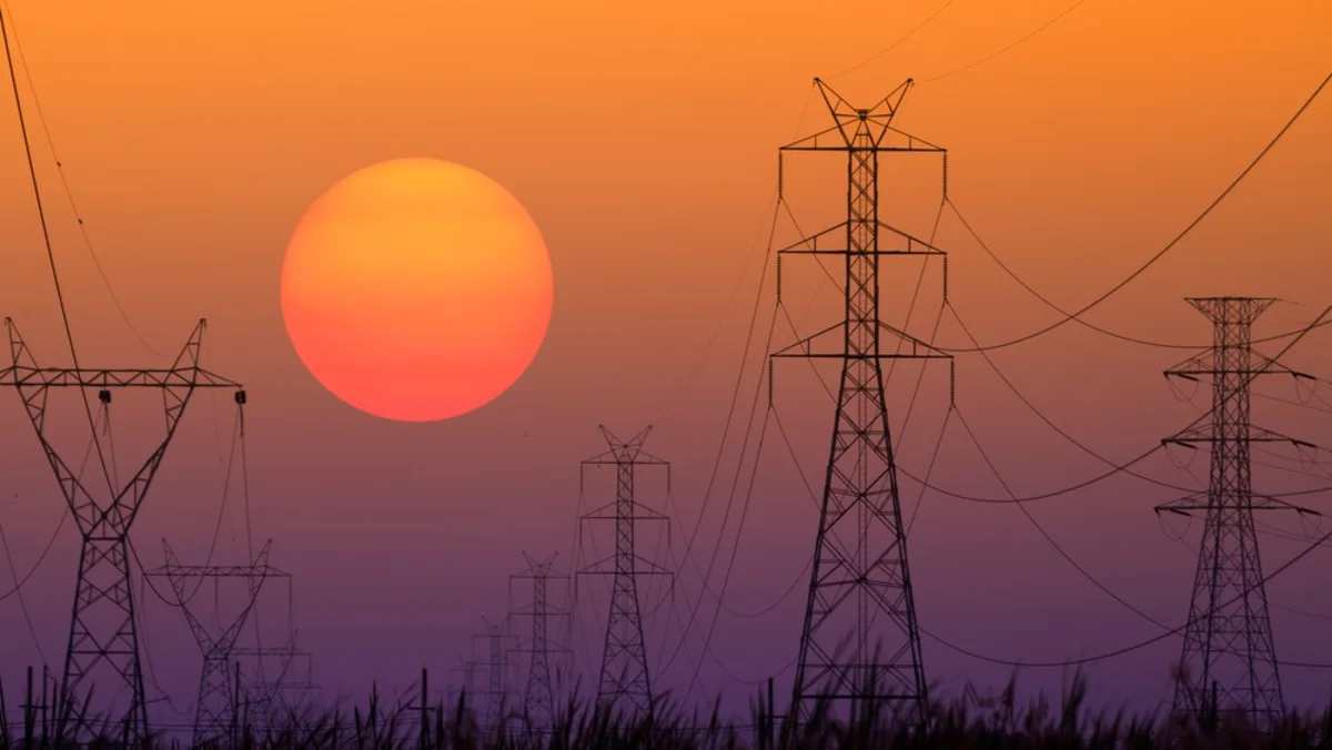 Power transmission towers and lines silhouetted against an orange-purple sunset with a large sun.