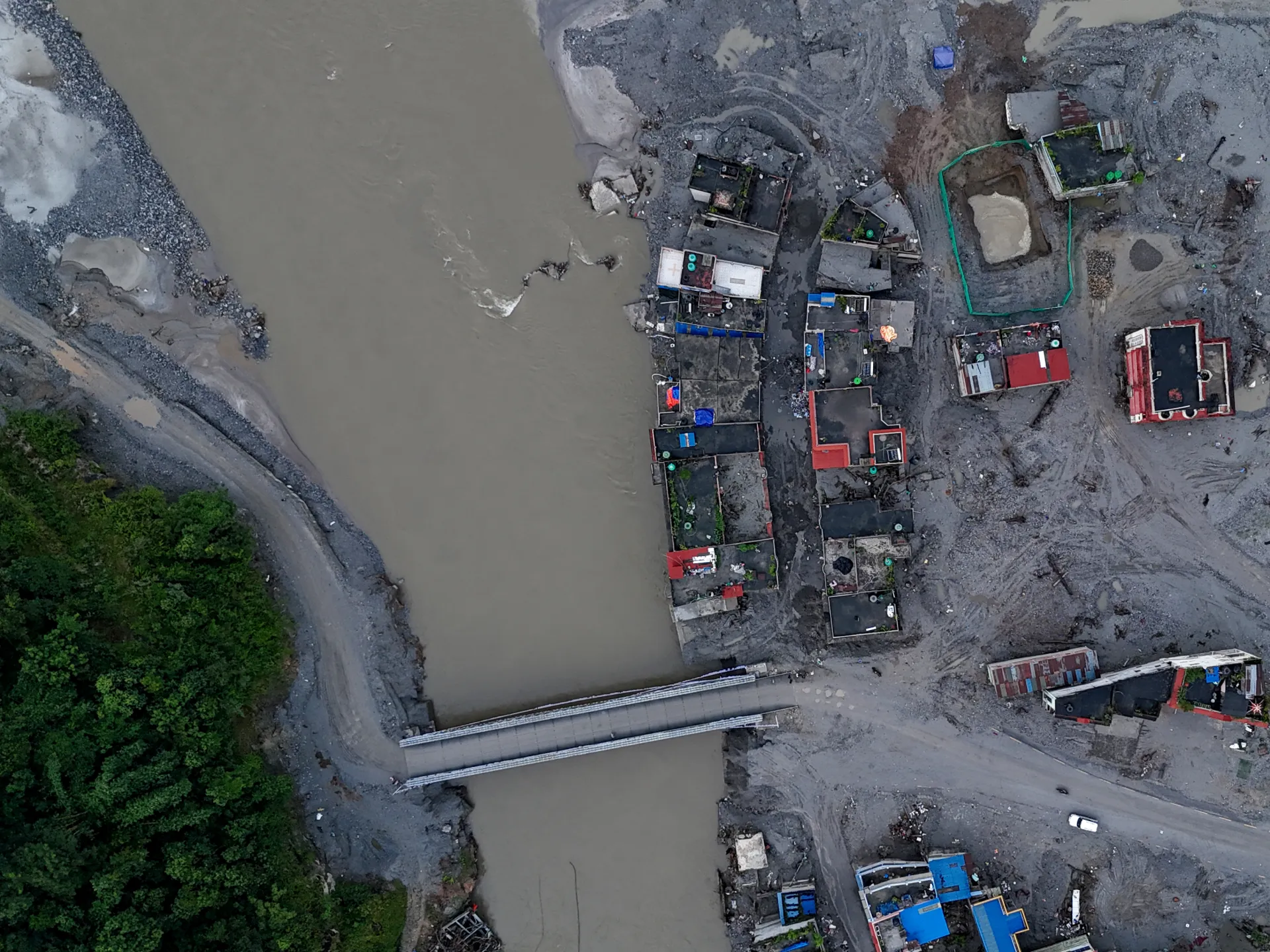 Aerial view of a muddy river, damaged bridge, and debris-covered buildings beside the banks.