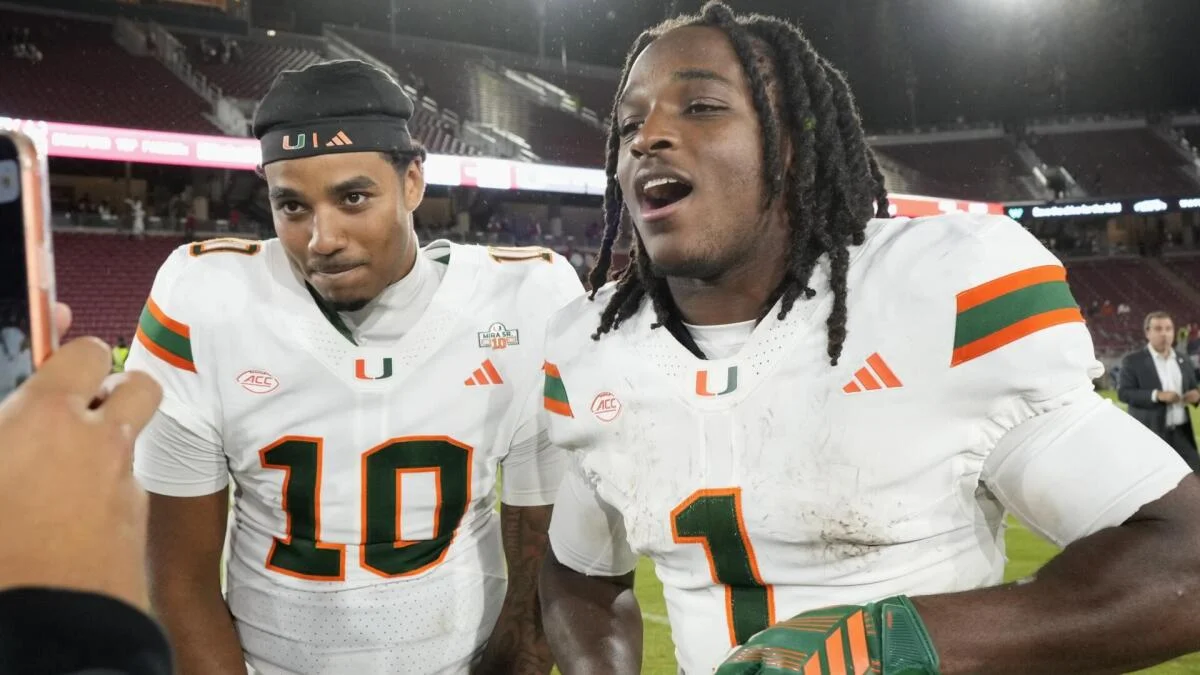 Two Miami football players in white uniforms pose together on the field after a game.