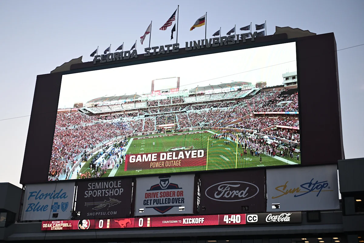 Large stadium video board displays "Game Delayed Power Outage" during a football game.