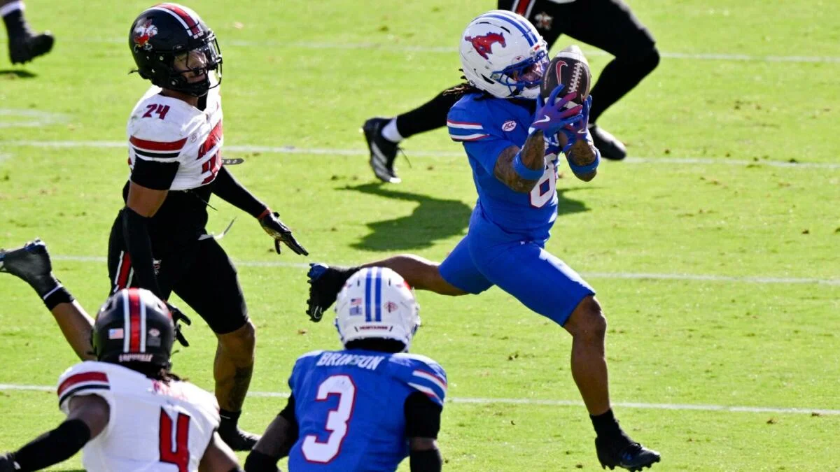 Football player in blue reaches for a pass as defenders pursue on a sunlit field