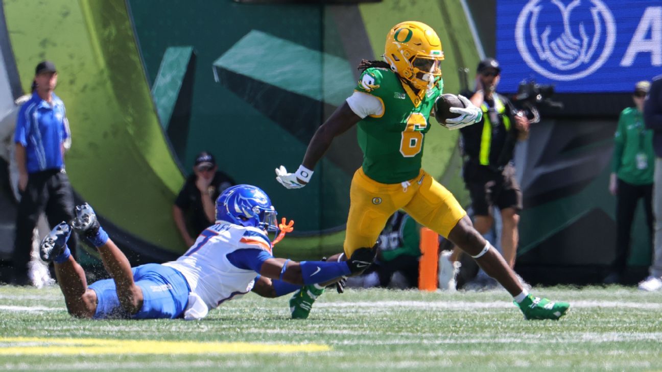 Oregon player in green and yellow runs with the ball as a Boise State defender dives.