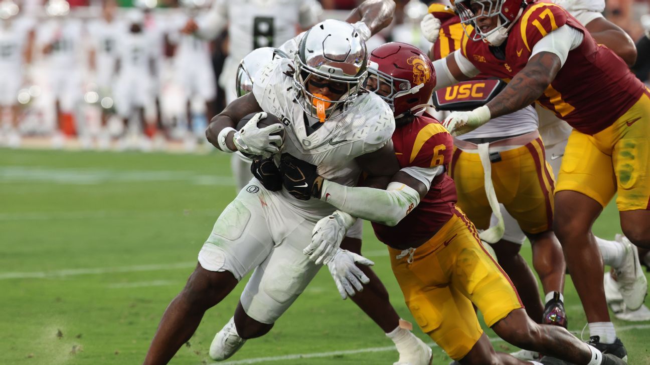 Oregon player in white carries the ball as USC defenders in cardinal and gold tackle him.