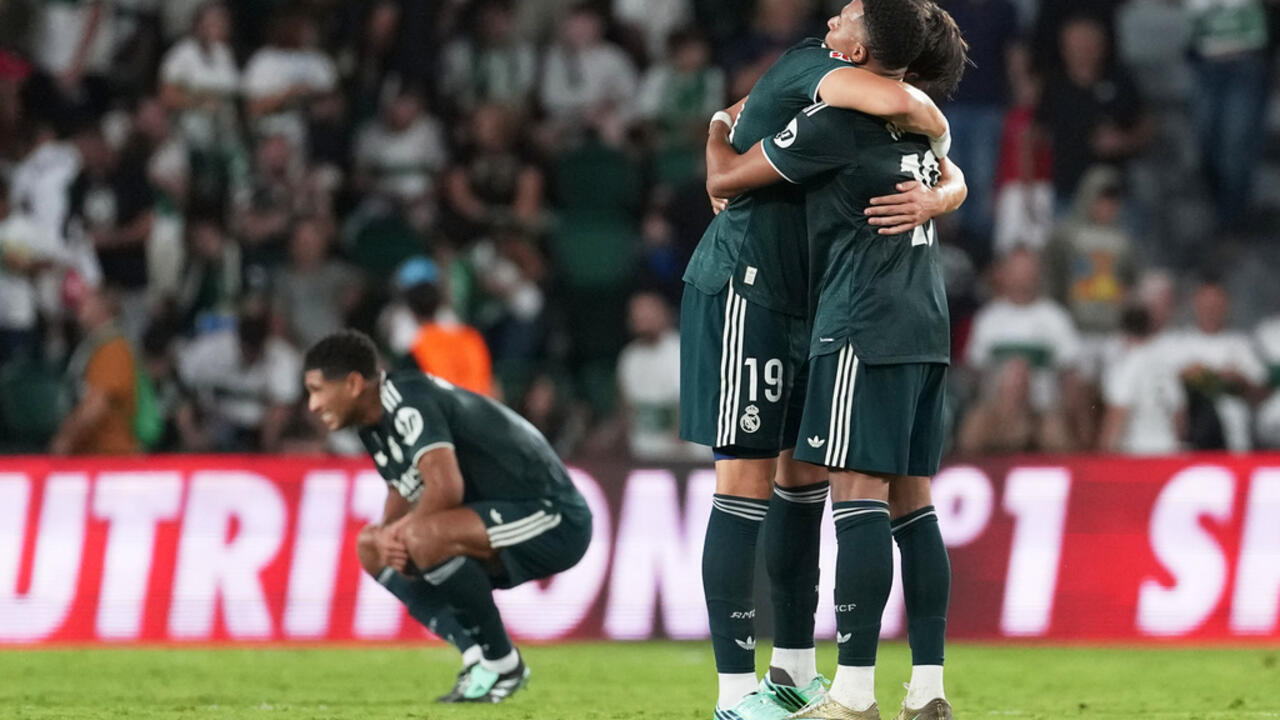 Real Madrid footballers embrace while a teammate crouches on the pitch during a match