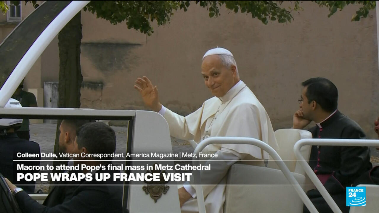 A white-robed cleric waves from a vehicle beside a seated cleric in dark clothing.