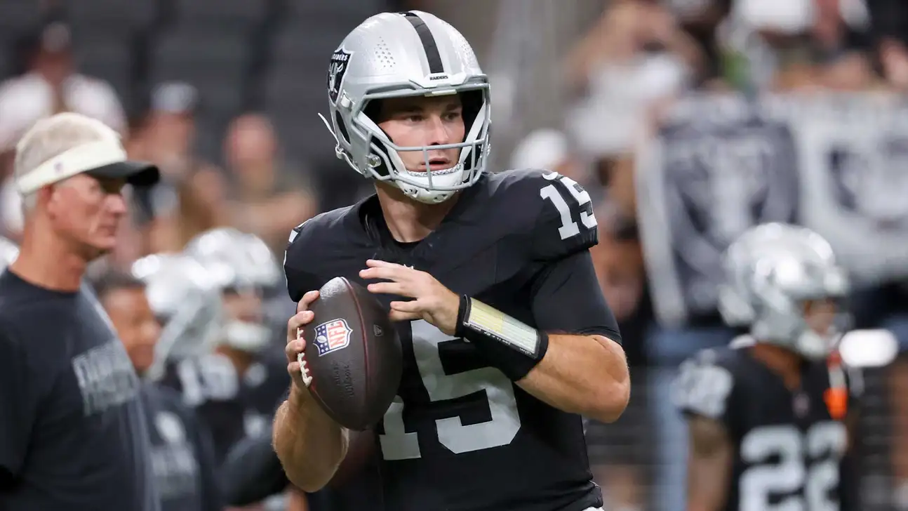 Football quarterback in Raiders uniform holding a ball during a preseason practice or game
