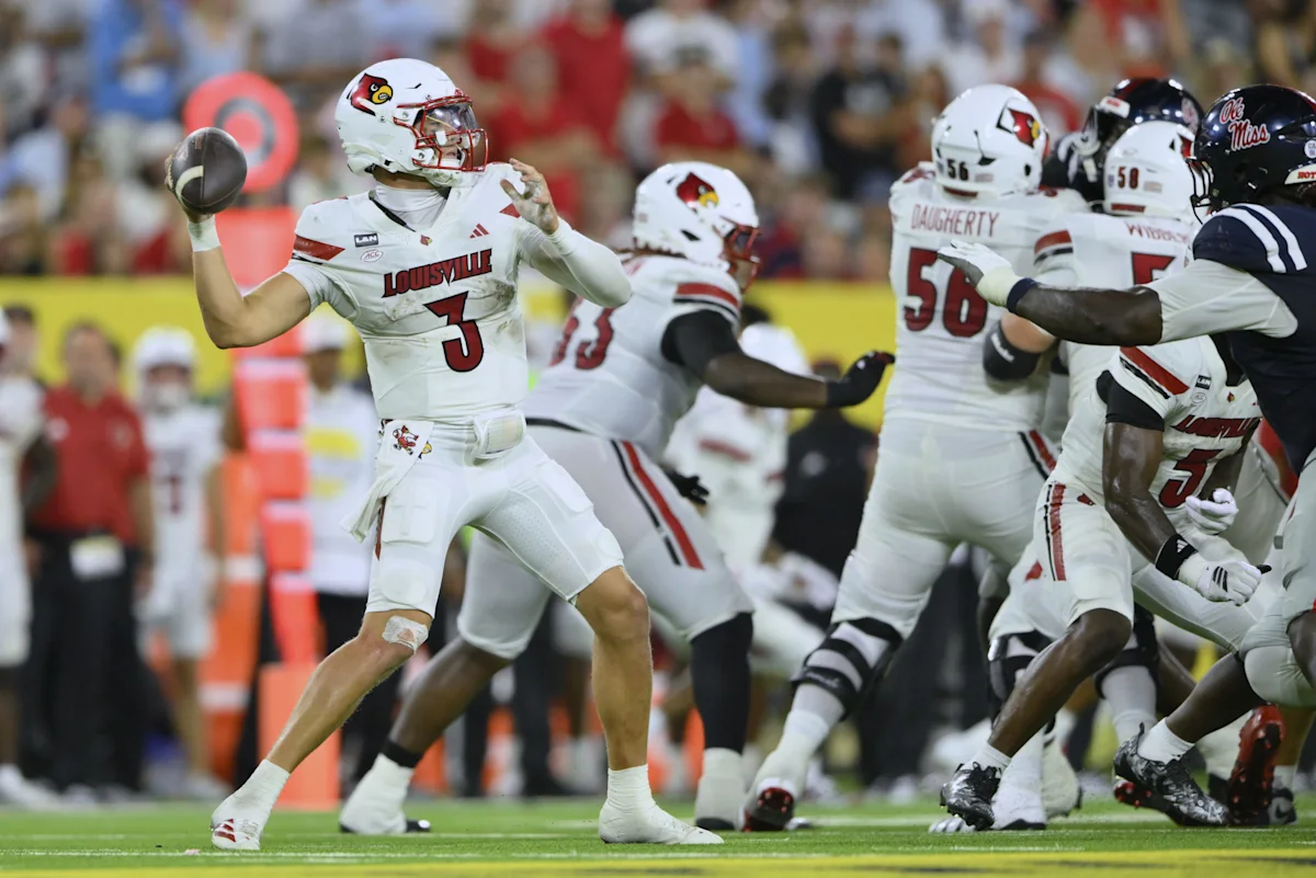 Louisville quarterback throws a football as teammates block defenders during a game.