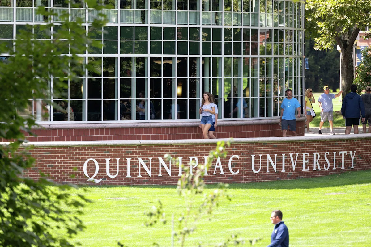 Quinnipiac University campus building with students walking beside a brick sign