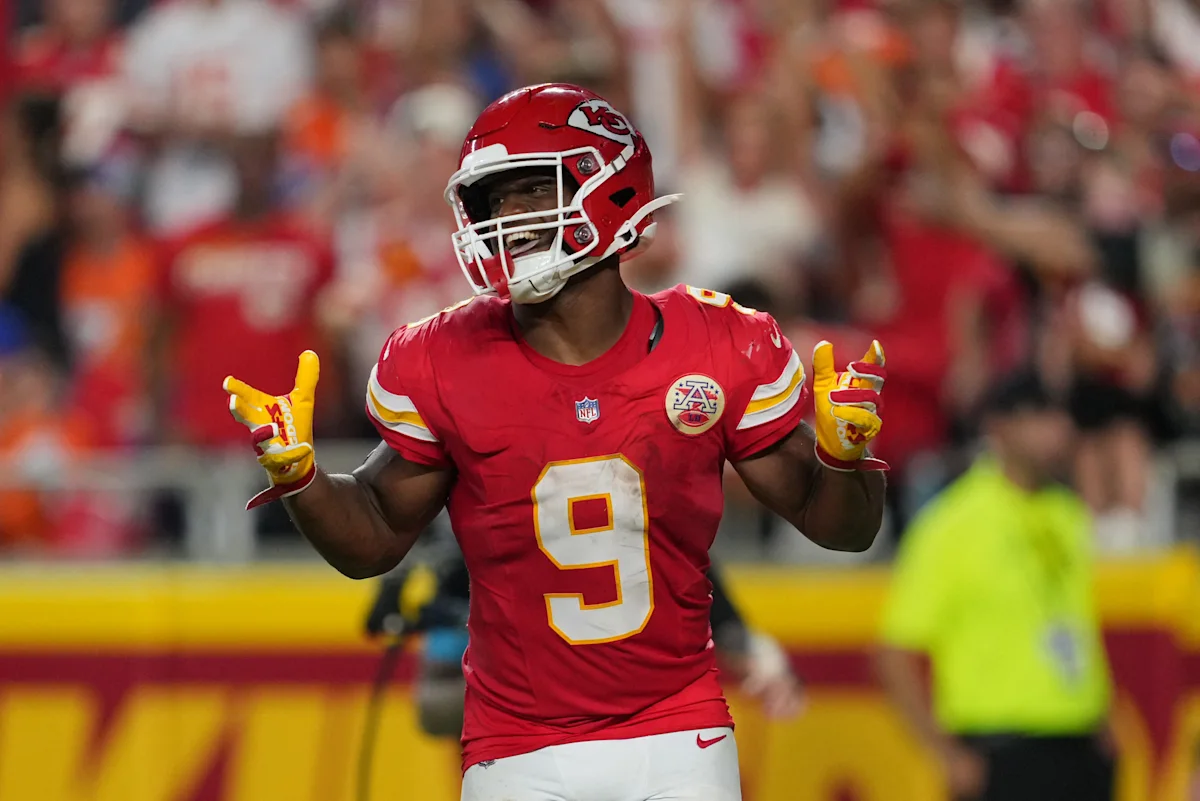 Football player in red Kansas City uniform celebrating with both hands raised