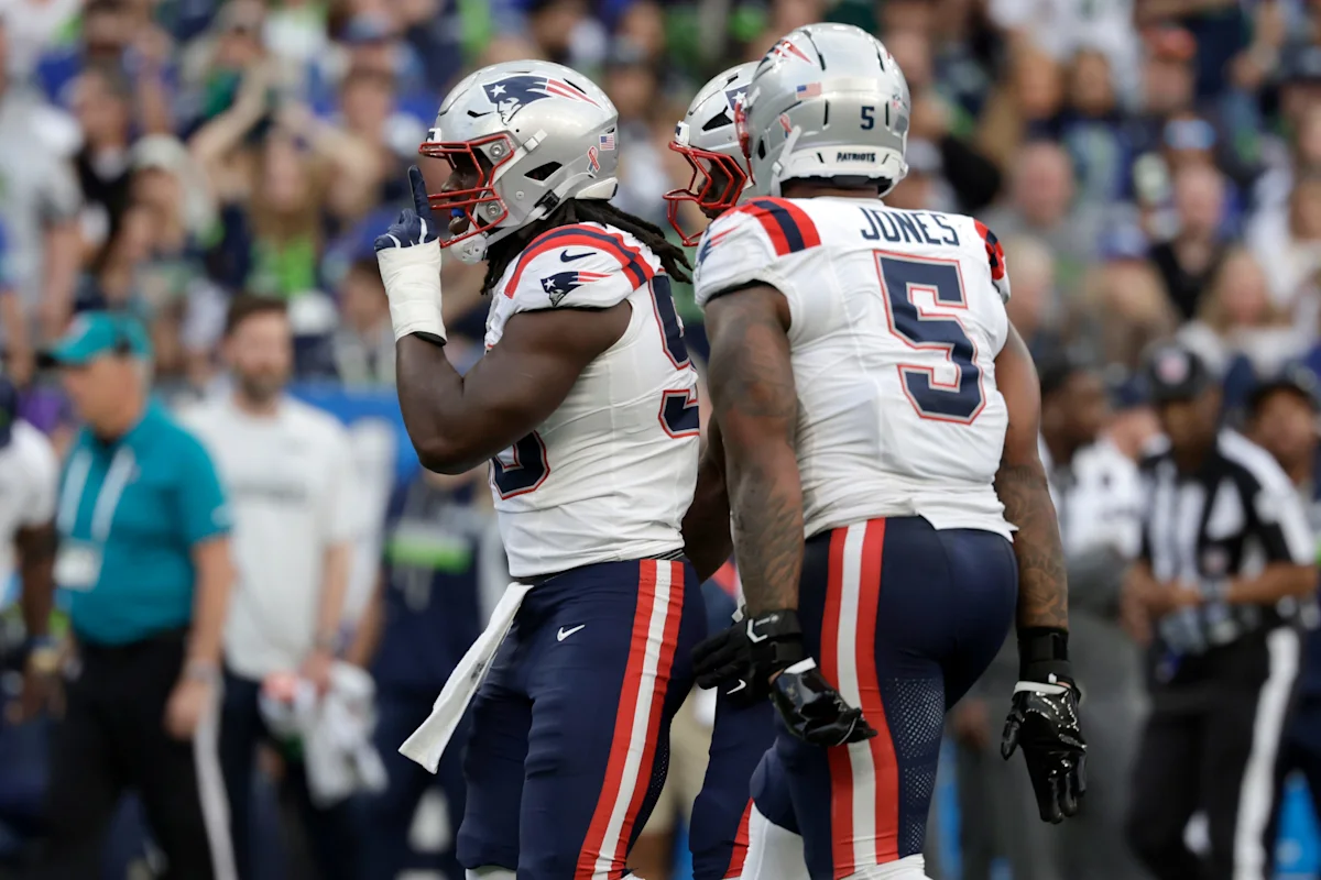 Two New England Patriots players in white uniforms and helmets stand together during an NFL game.