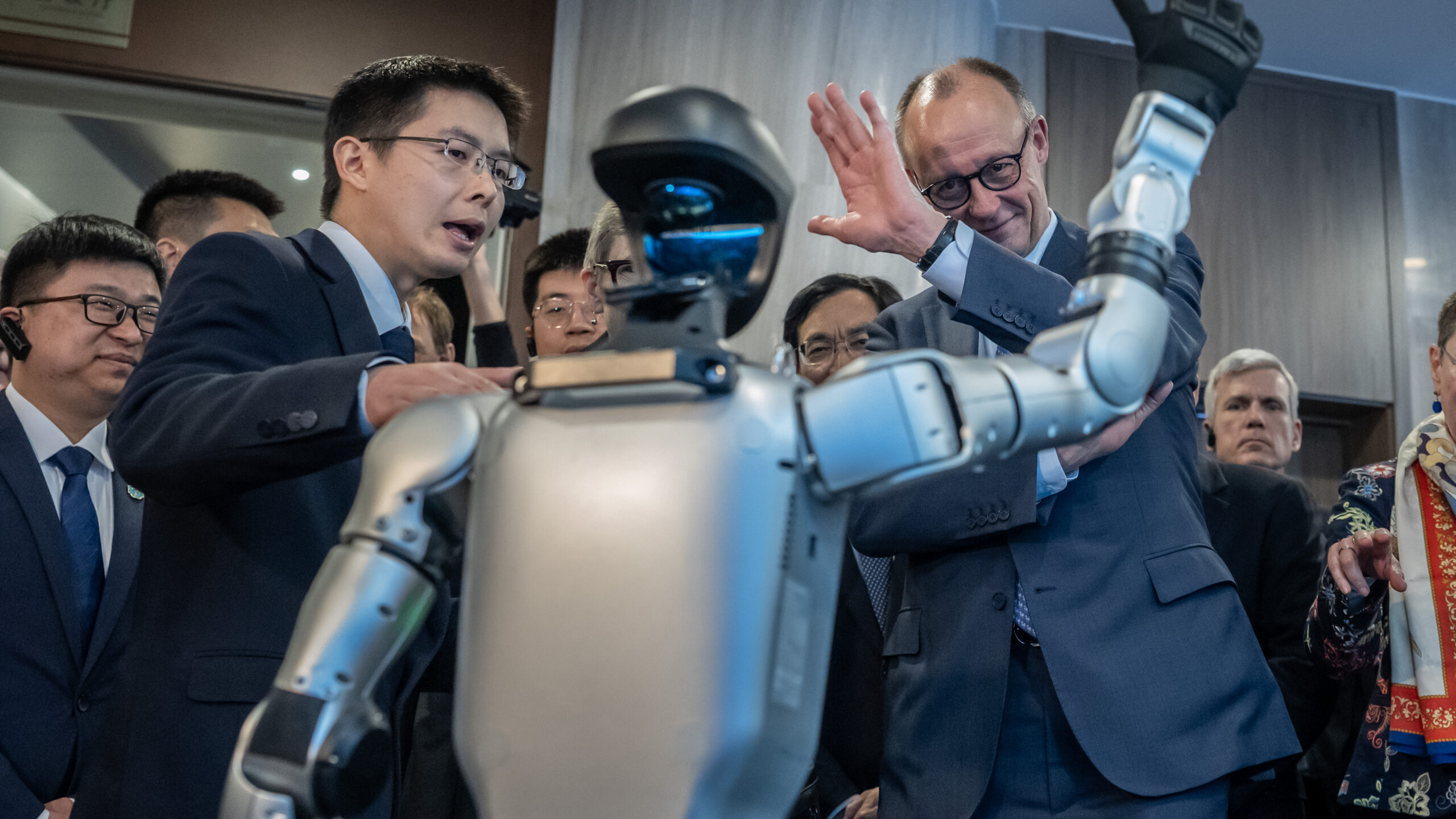 A humanoid robot stands amid suited officials and attendees during a crowded demonstration.