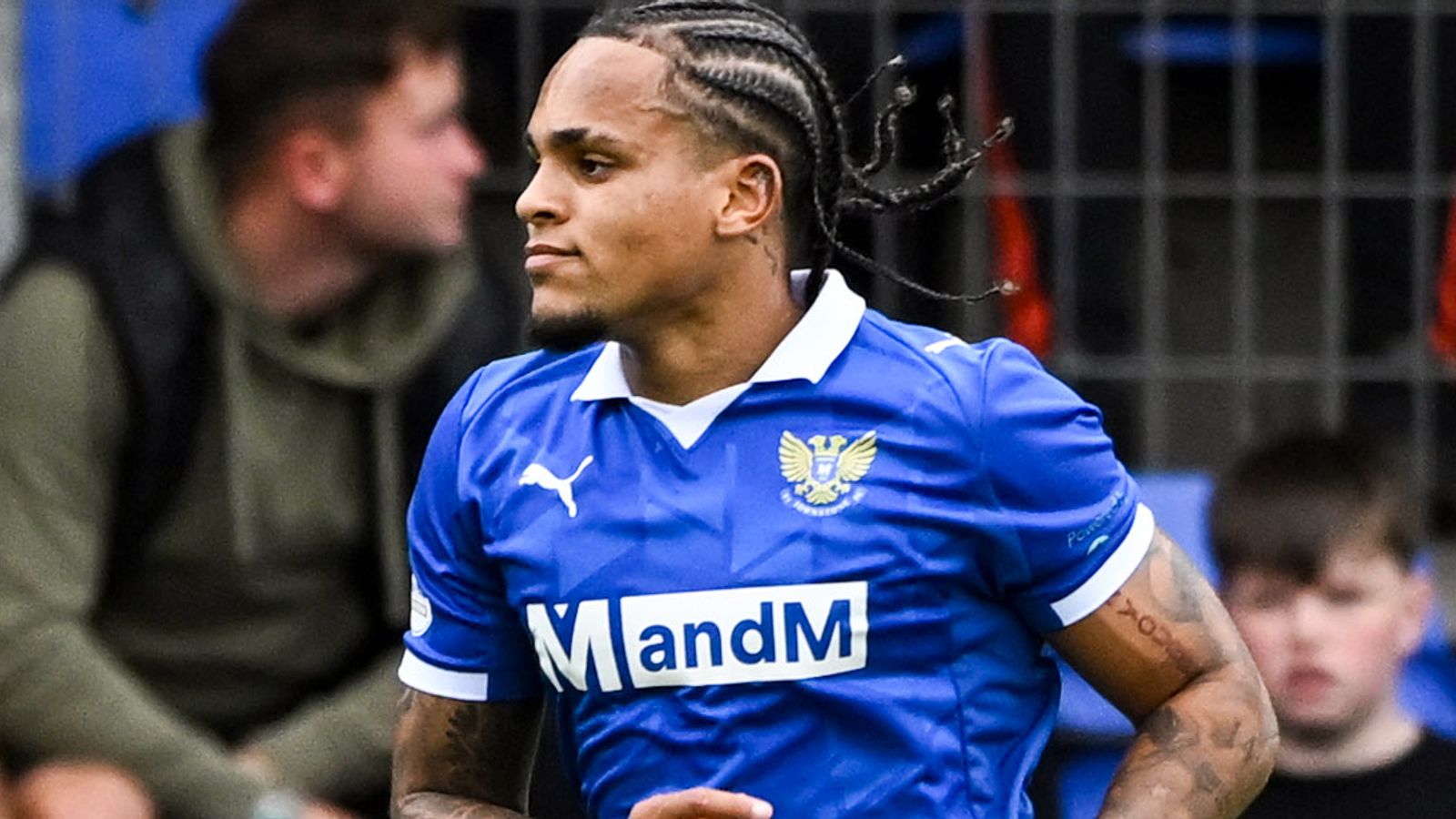 Footballer with braided hair in a blue jersey runs during a match.