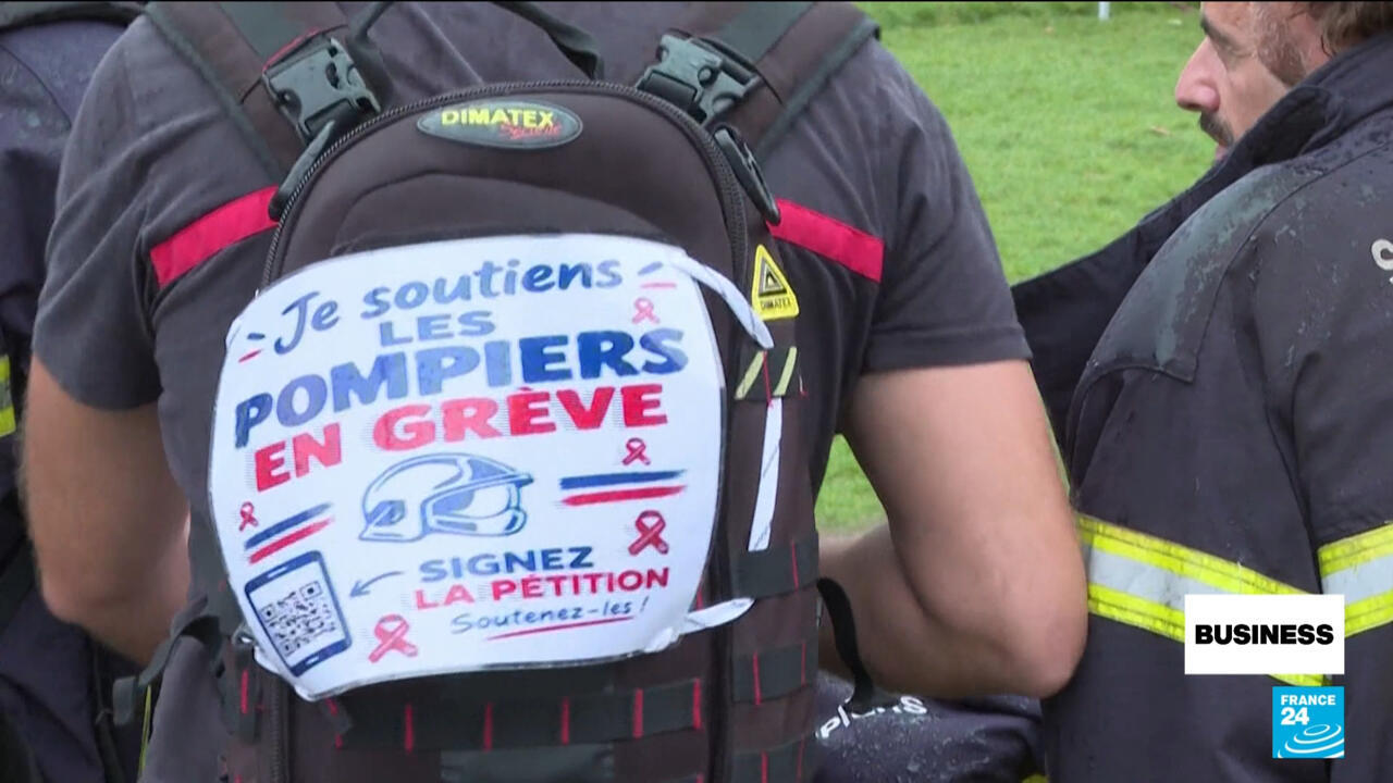 A firefighter wears a backpack displaying a French strike petition poster calling for support for firefighters.
