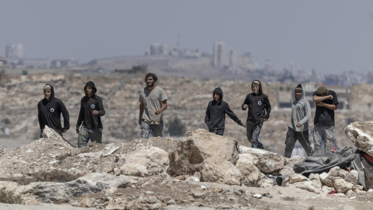 People walk across rubble-strewn ground with a hazy urban skyline in the background.