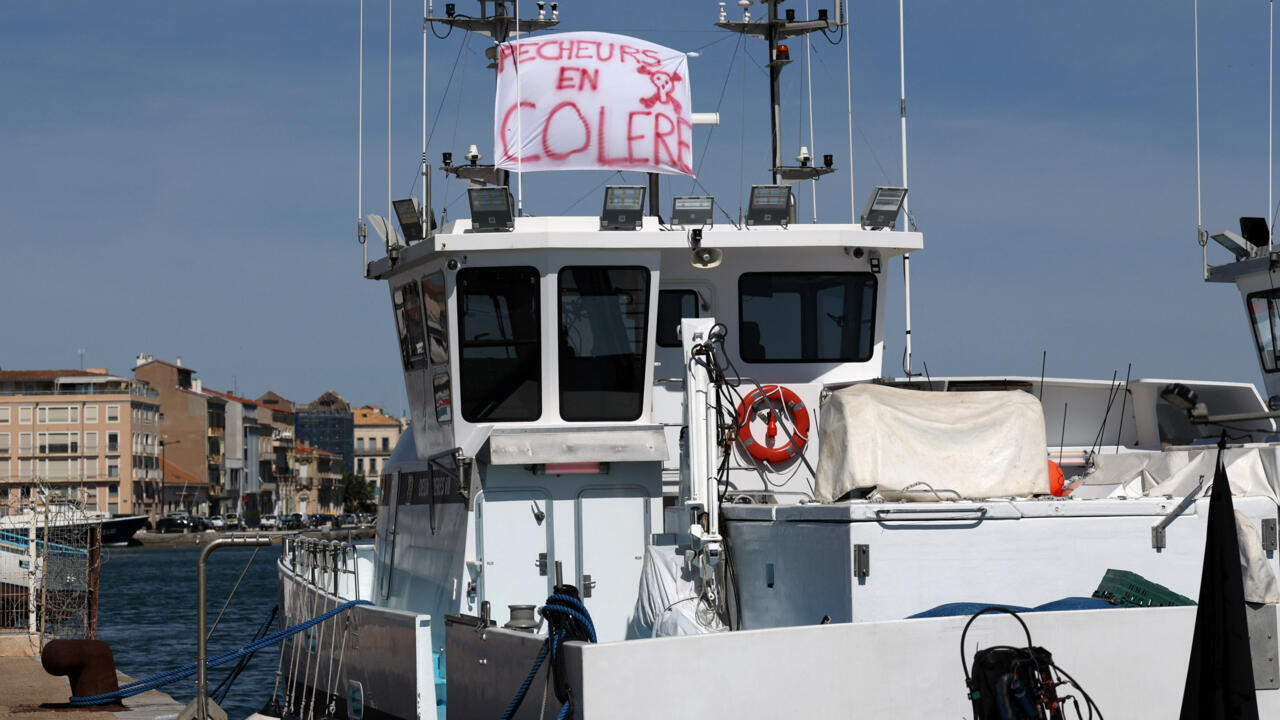 Fishing boat displaying a protest banner reading “Fishermen in anger” in a harbor