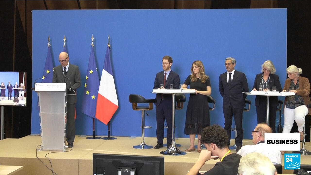 Officials stand beside European Union and French flags during a government press event.