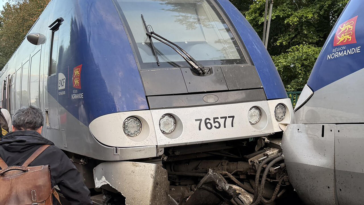 Damaged blue regional train pressed against another train, with debris visible between the locomotives.