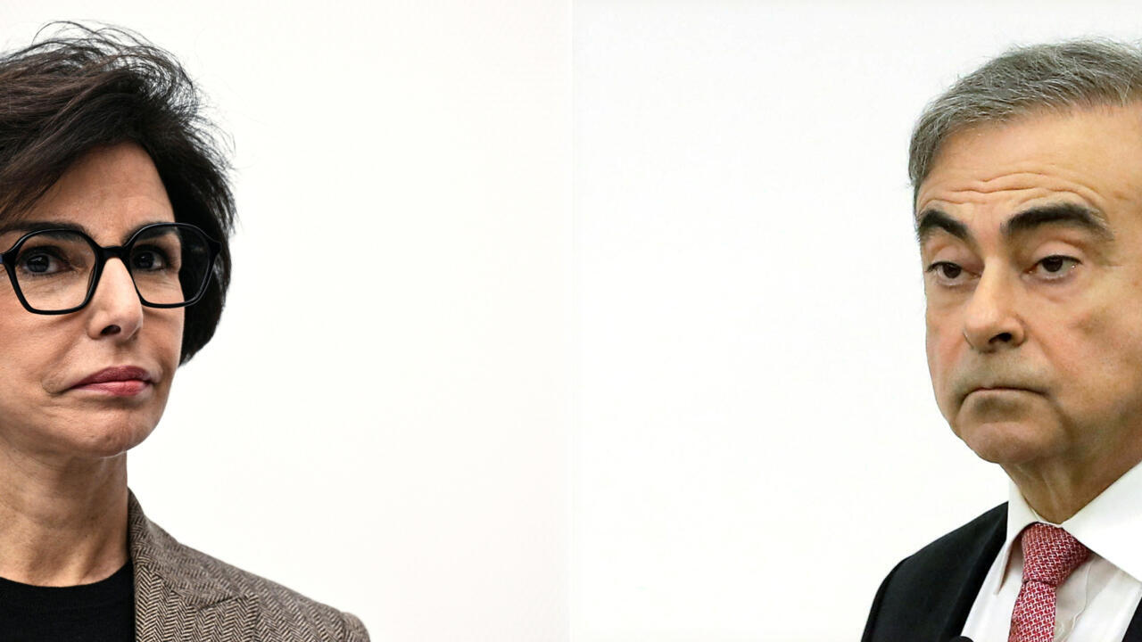 A woman in dark glasses and a man in a suit face forward against a plain white background.