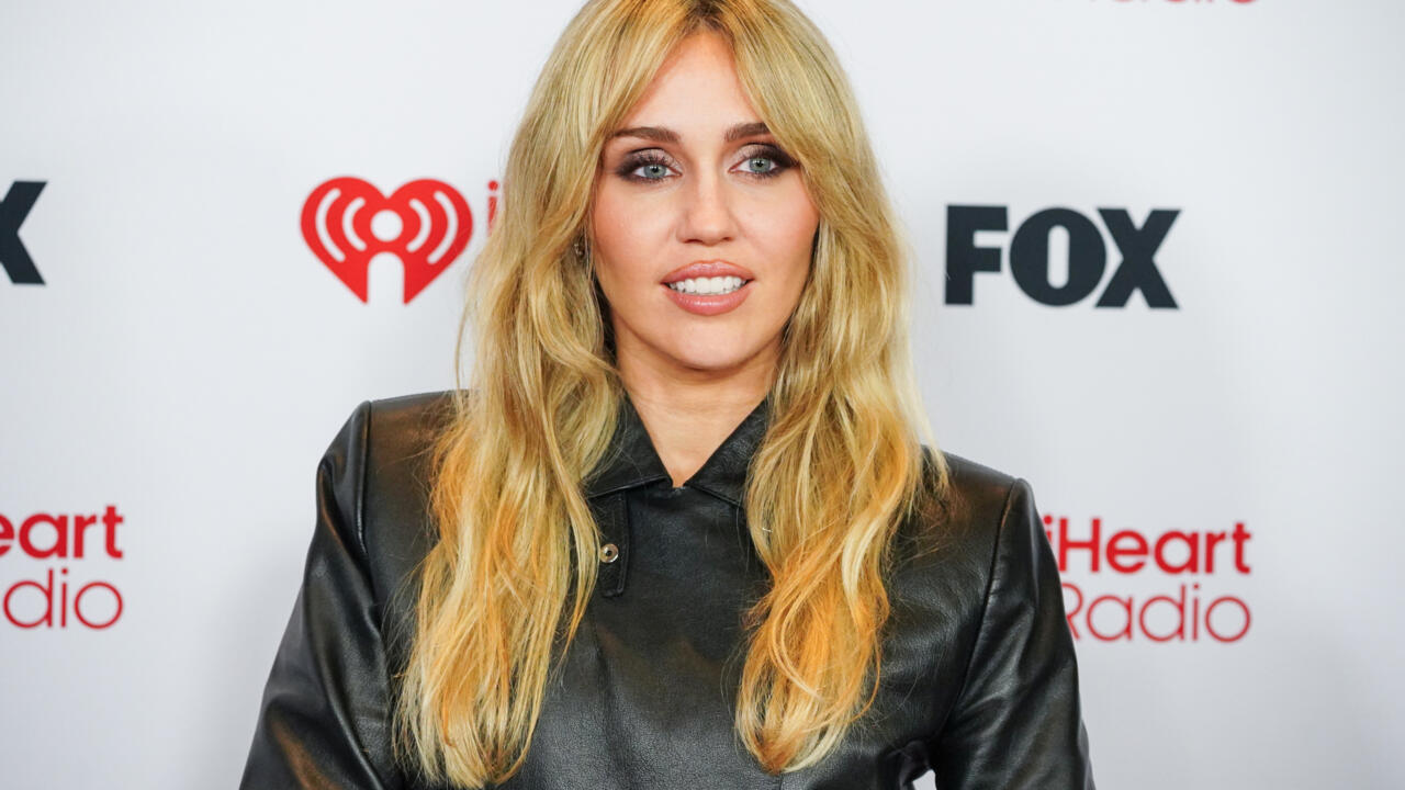 Blonde woman in black leather shirt posing before iHeartRadio and FOX media logos