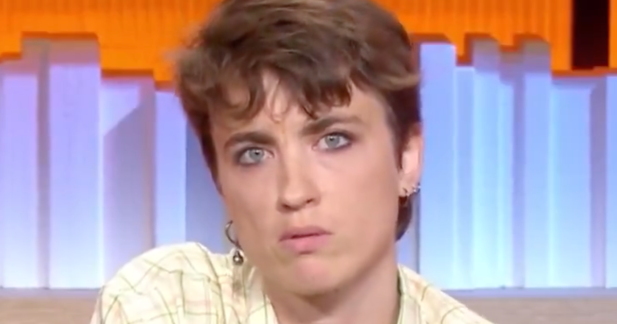 Close-up of a short-haired person with blue eyes and earrings looking seriously toward the camera