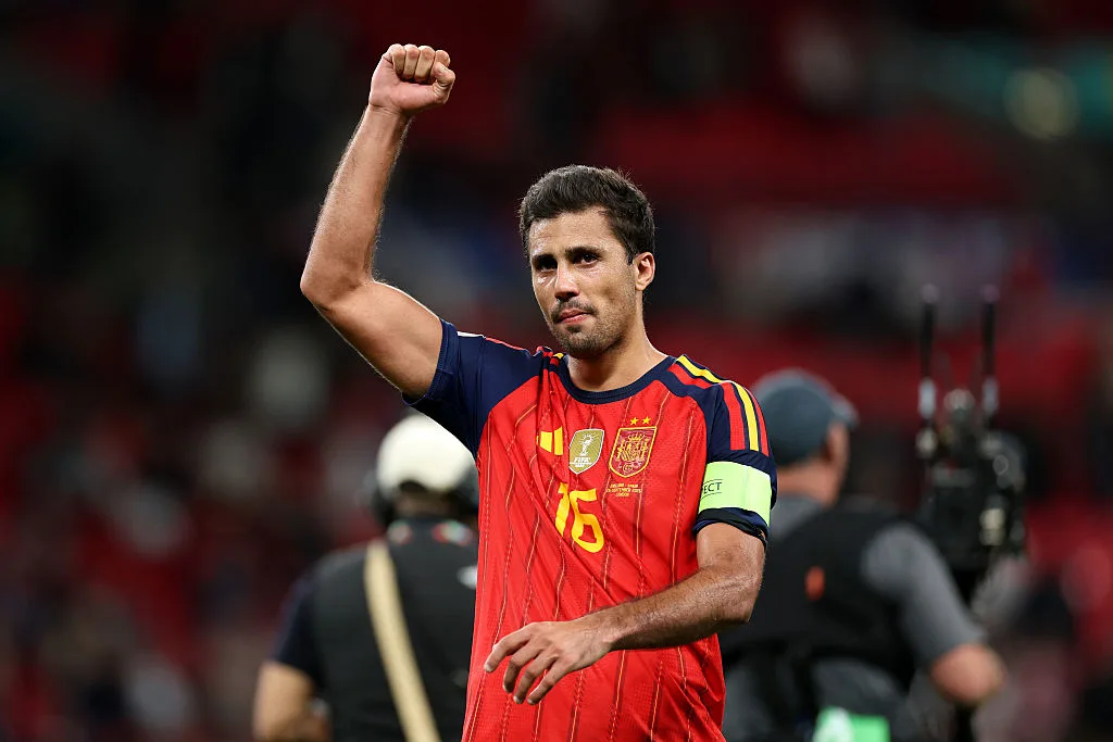 A Spanish footballer in a red jersey raises his fist in a stadium.