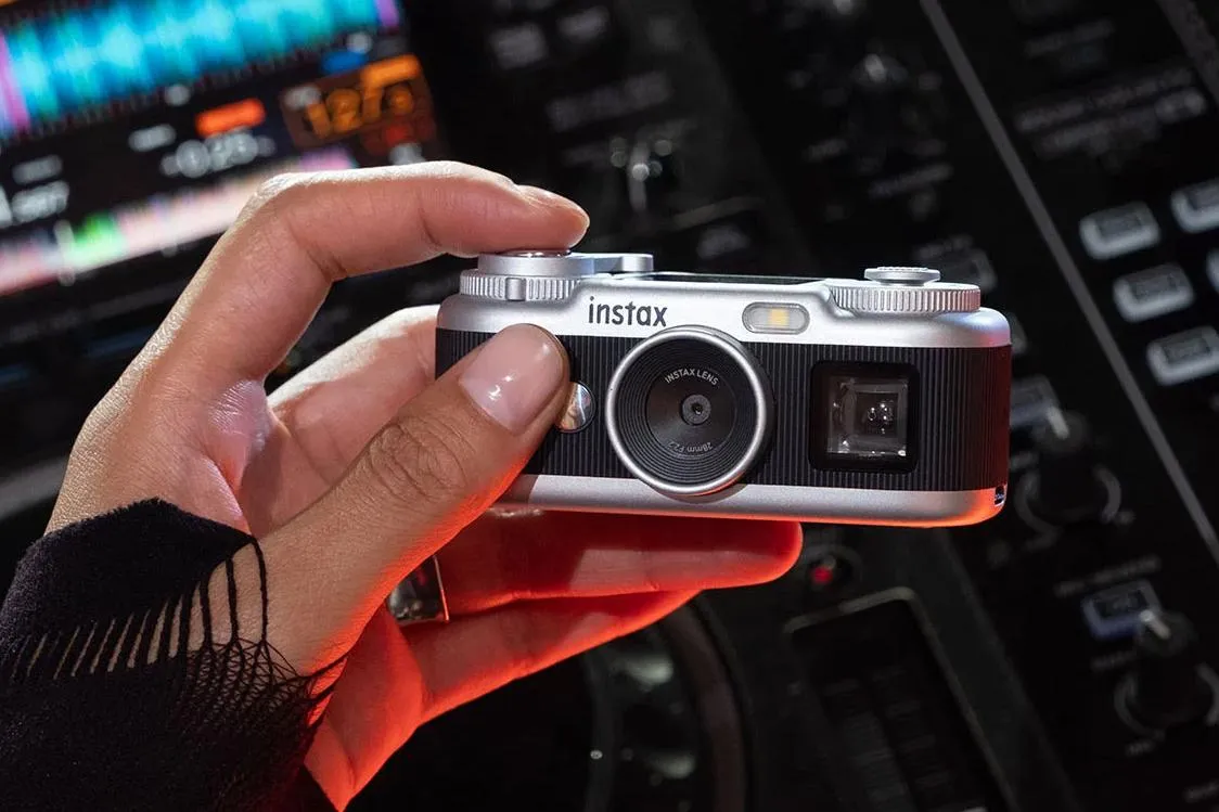 Hand holding a silver Instax camera against a blurred car dashboard at night.