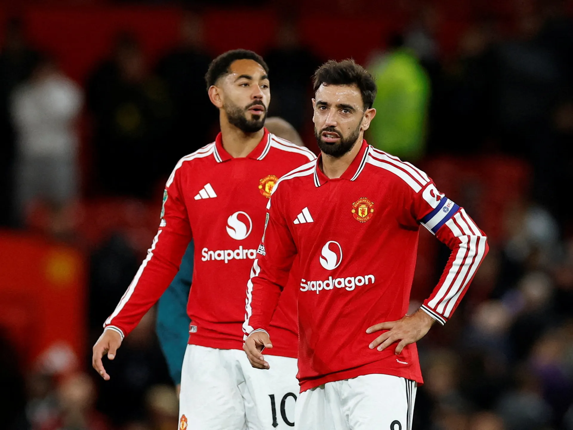Two Manchester United players in red kits stand on the pitch during a match.