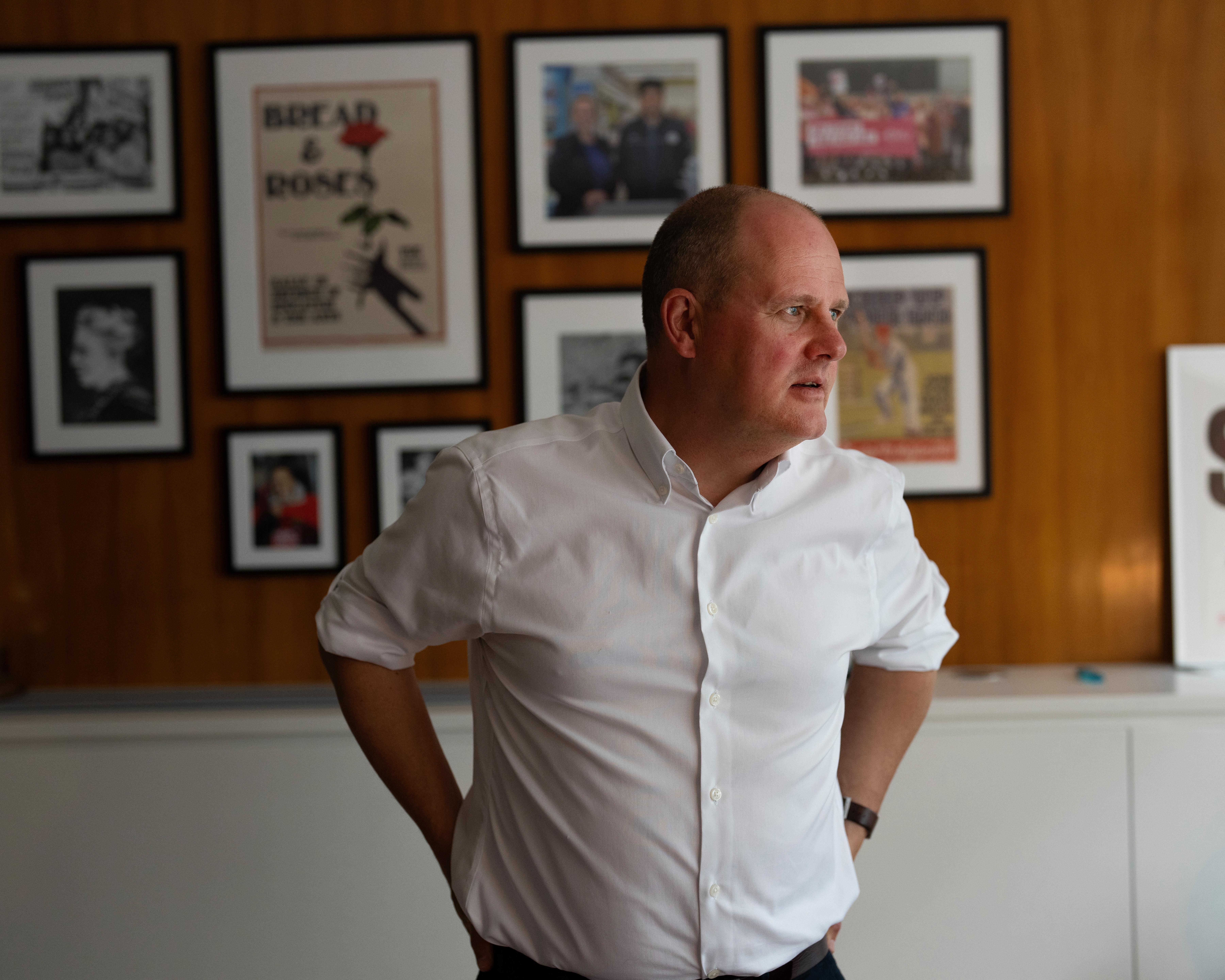 Man in white shirt standing before framed photographs on a wood-panelled wall