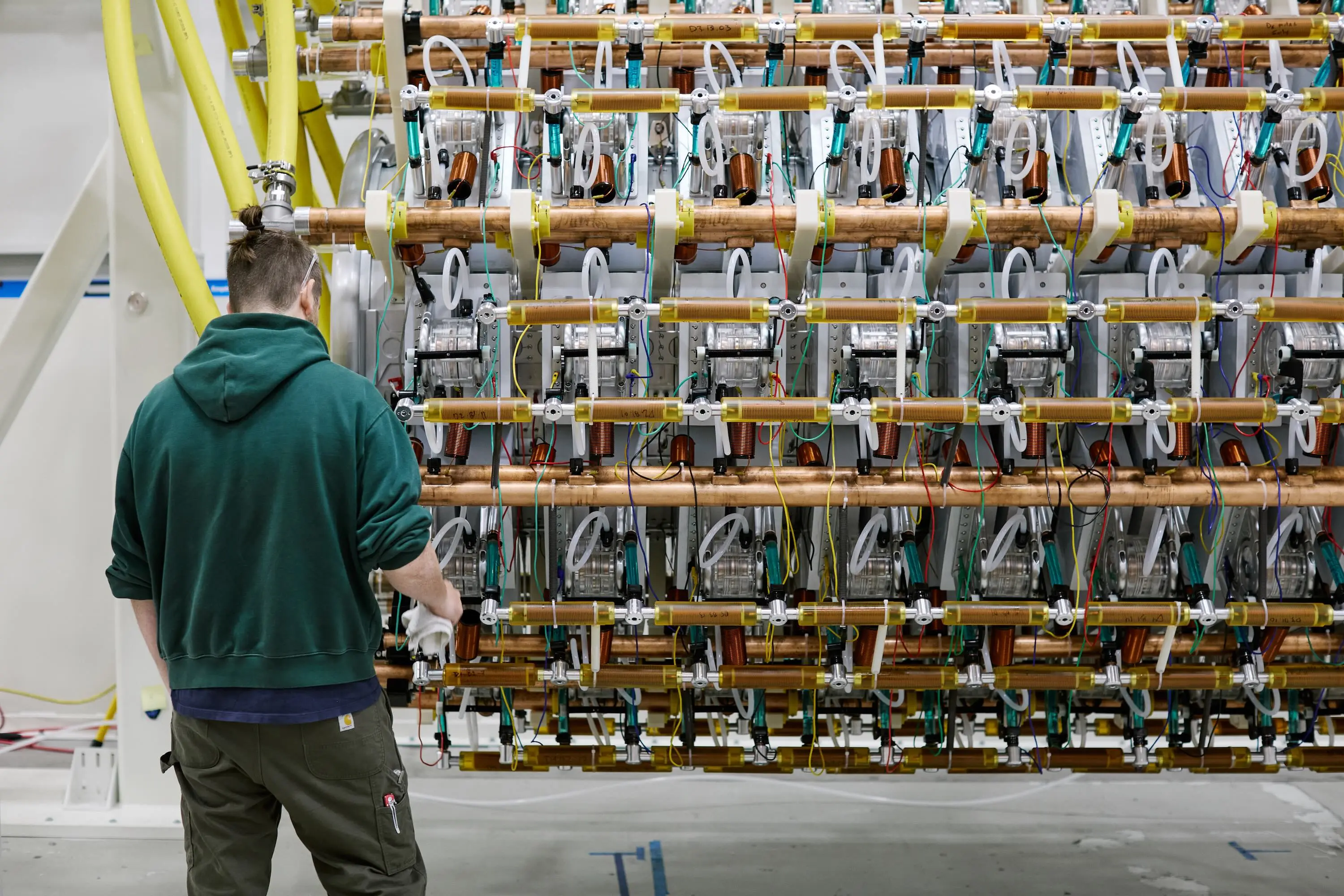 Worker examines a large laboratory apparatus of copper pipes, coils, wires, and transparent tubing.