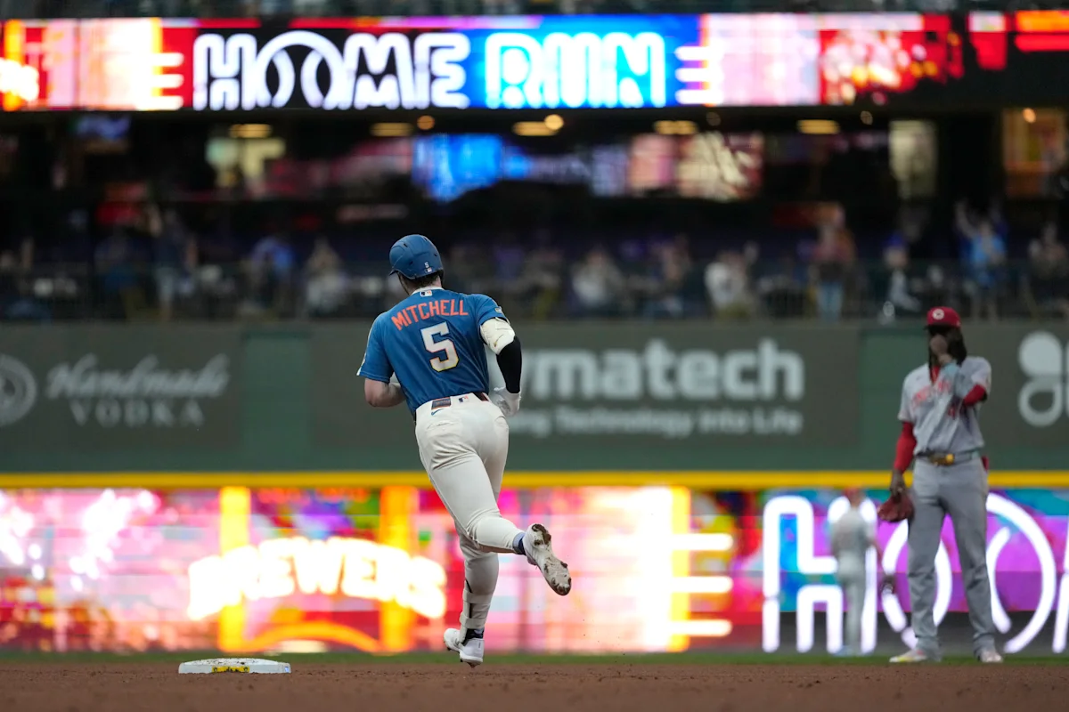 Brewers player wearing number 5 rounds a base as a Reds fielder watches.