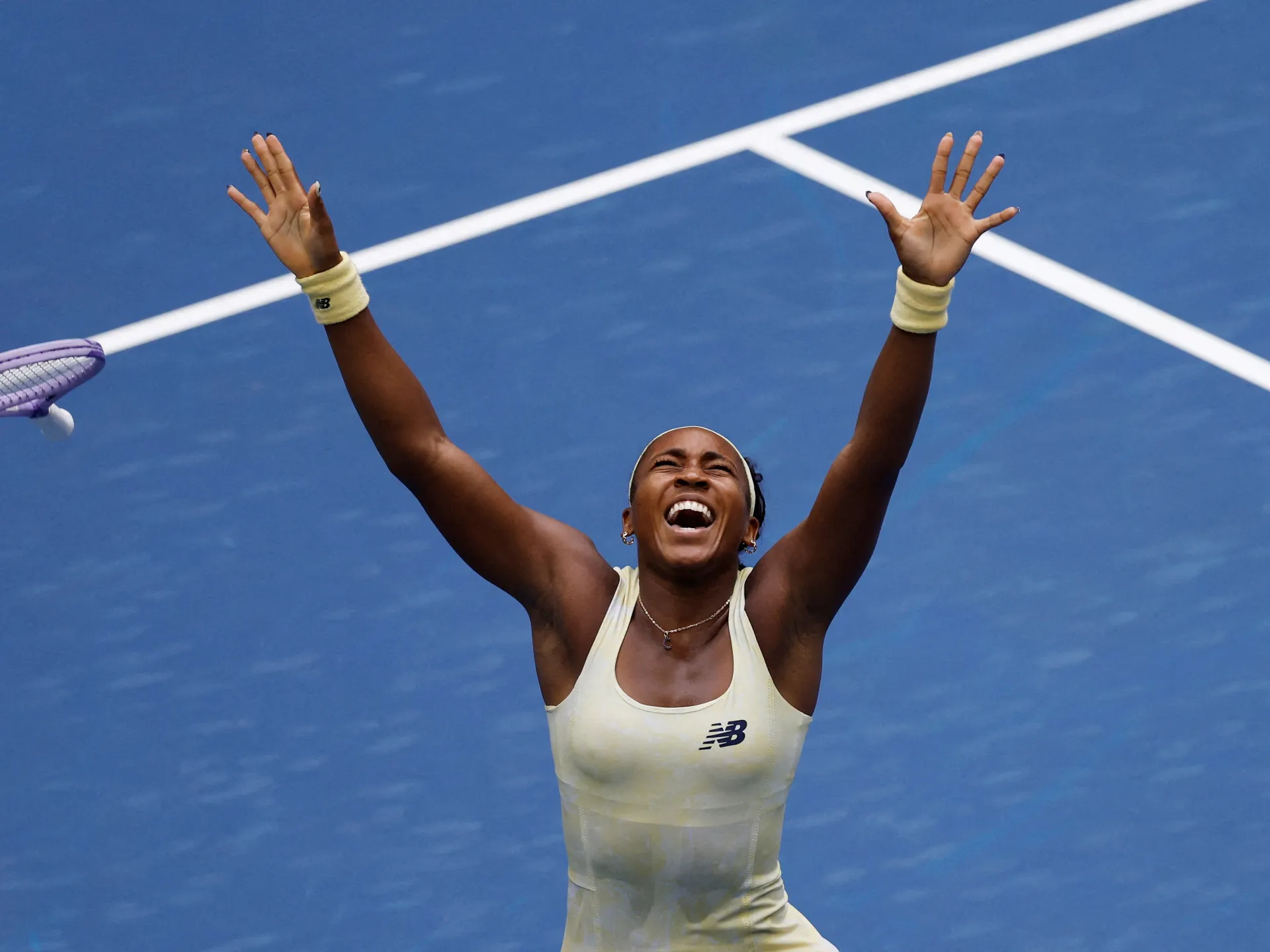 Tennis player celebrates with arms raised on a blue court after winning a match