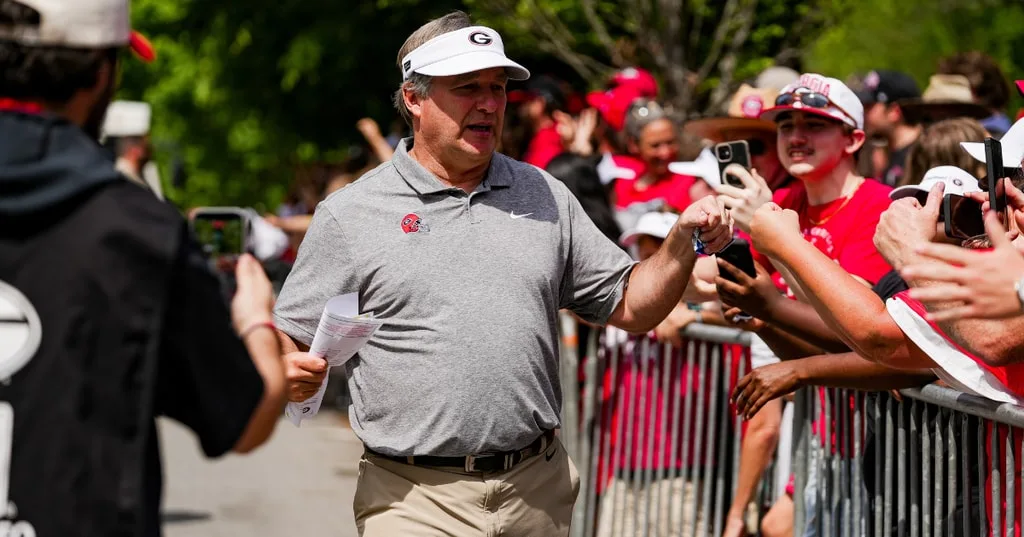 Georgia coach in visor greets fans behind a metal barricade outdoors