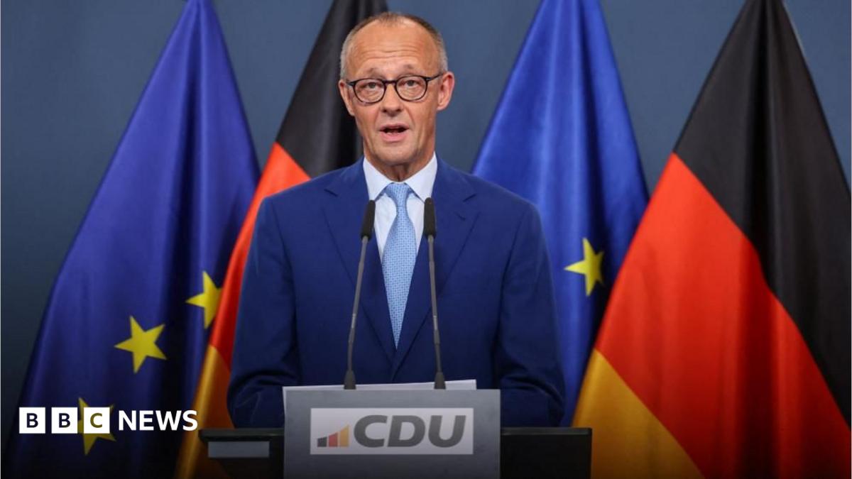 German politician speaking at a podium with European Union and German flags behind him