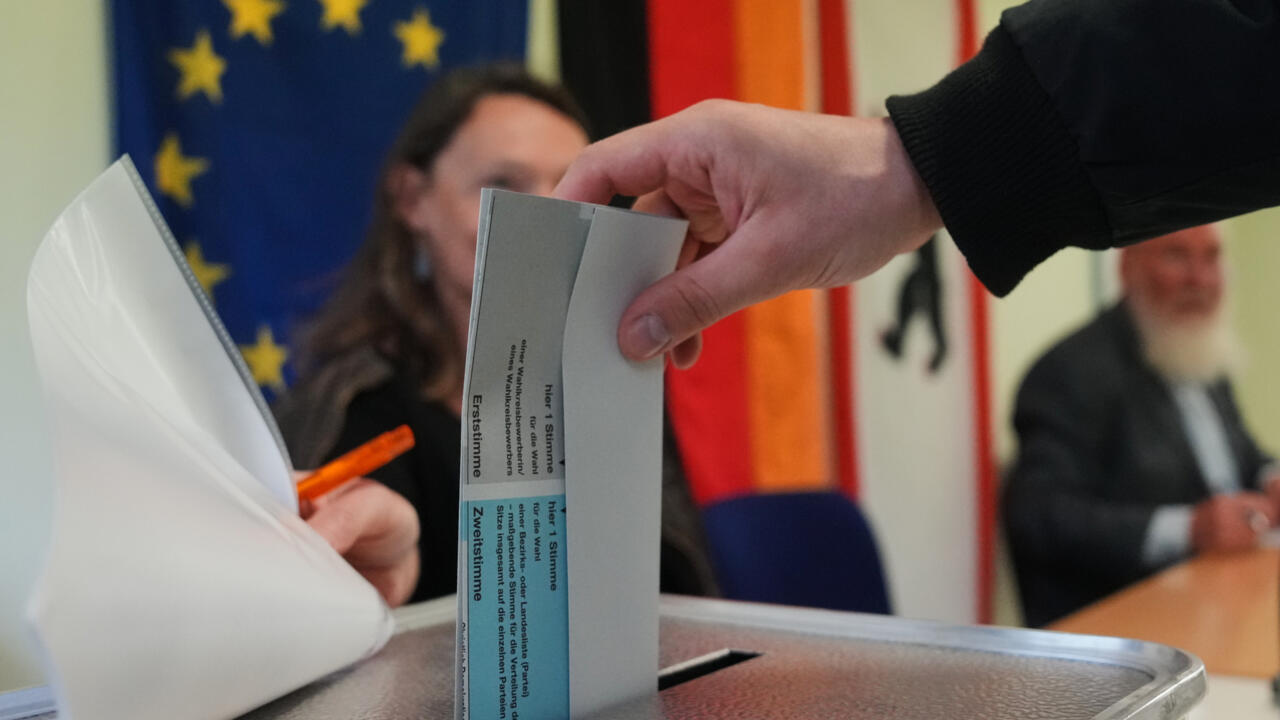 Hand placing a ballot paper into a transparent ballot box during an election