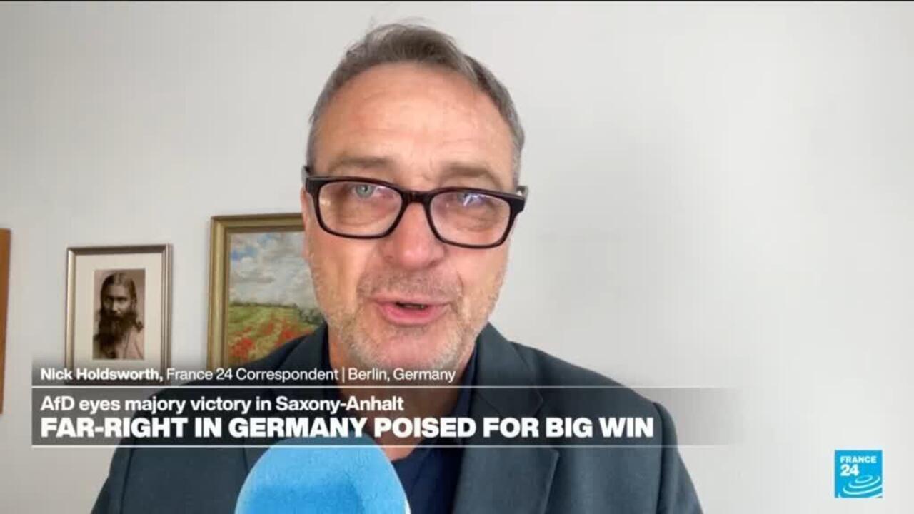 Television correspondent wearing glasses speaks into a blue microphone during a France 24 news broadcast.