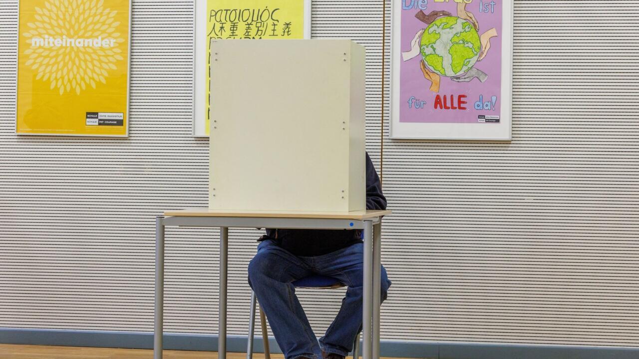 Person seated behind a privacy voting booth in a polling station with posters on the wall