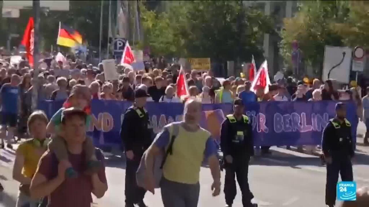 Crowd marches behind a purple banner as police officers monitor a street demonstration.