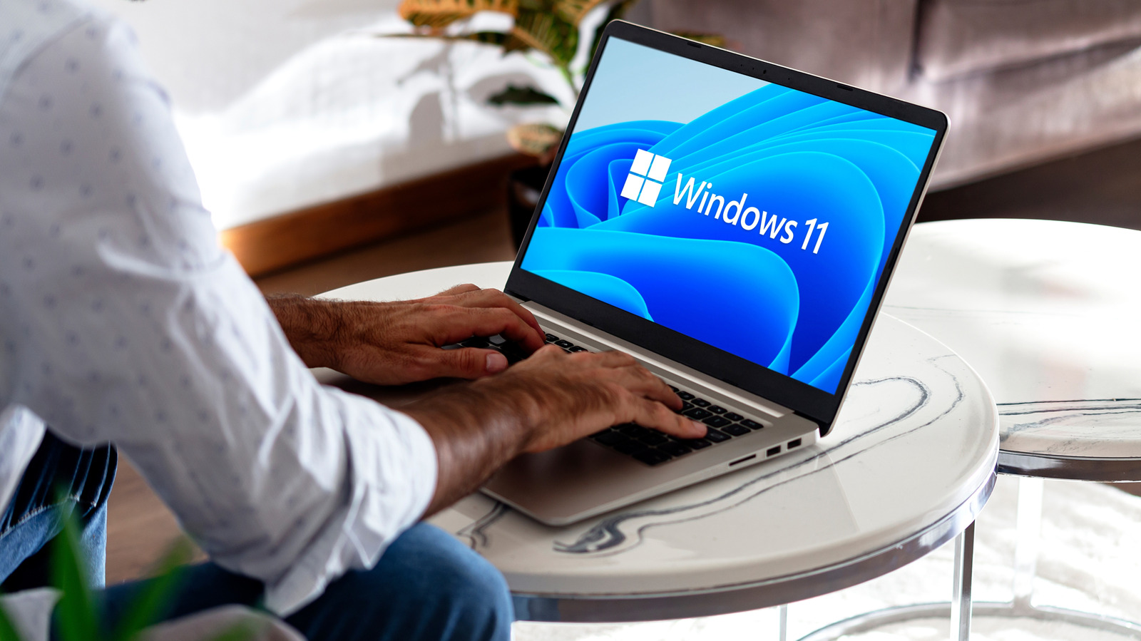 Person typing on a laptop displaying the Windows 11 logo at a round table