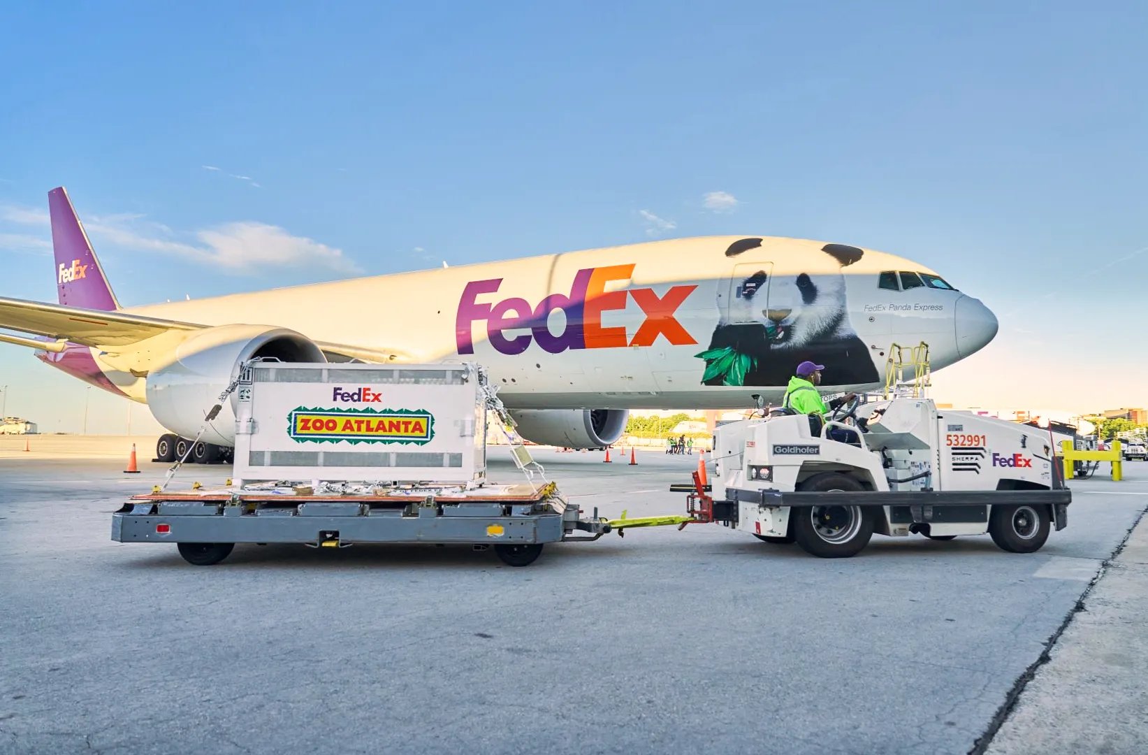 A FedEx cargo plane with panda artwork sits behind a ground vehicle towing a Zoo Atlanta crate.