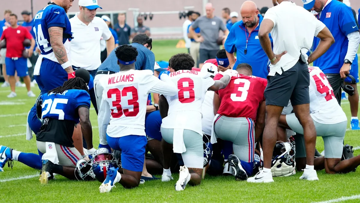 Football players and staff kneel around a teammate during a practice stoppage.