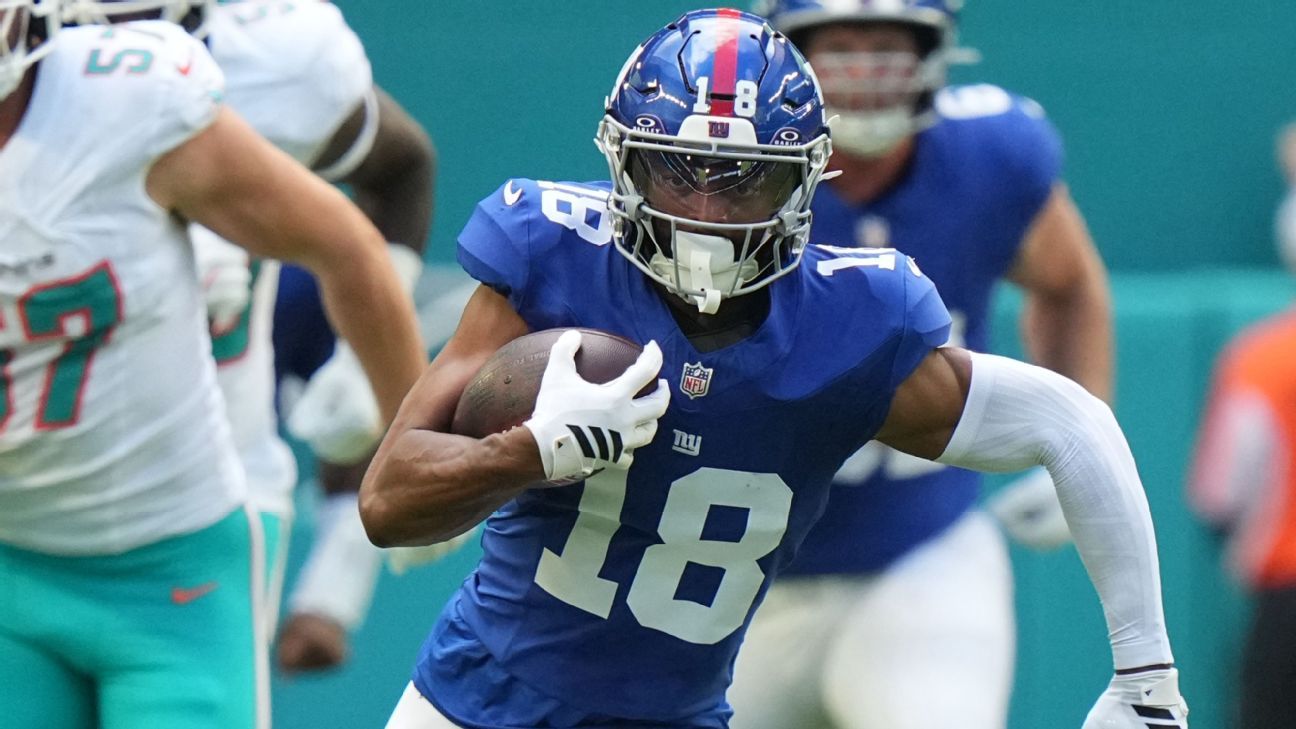 New York Giants player in blue uniform runs with football while evading defenders